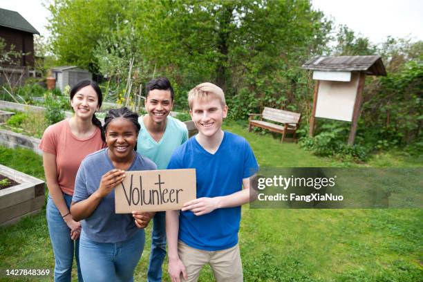 multiracial group of young men and young women stand together and hold volunteer sign within community garden park in neighborhood - 青少年組織 個照片及圖片檔