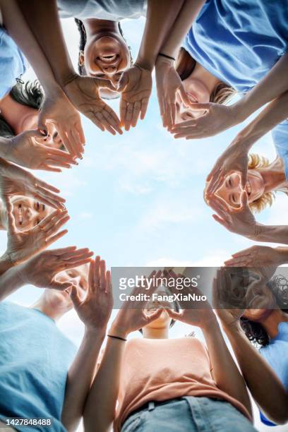multiracial group of diverse people stand in circle as community volunteers to show support and commitment to teamwork success togetherness making hand gesture in concept symbol sign of heart shape outdoors with sky - multiculturalism 個照片及圖片檔