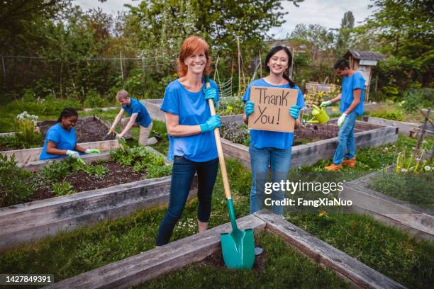 young asian woman holds thank you sign together with mature woman project manager leader standing in community garden park in support teamwork togetherness with multiracial group of diverse volunteers in neighborhood - nutrition coach stock pictures, royalty-free photos & images