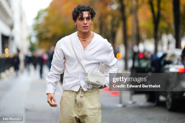 Guest wears a white pearls necklace, a white wool cardigan, a pale gray fabric crossbody bag, yellow pants, outside Jacquemus, during Paris Fashion...
