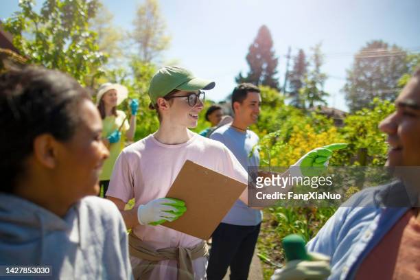 young man student coordinates as manager leader the cleanup work for youth organization volunteer charity in local community garden public park in residential district in summer - organisation environnement stockfoto's en -beelden