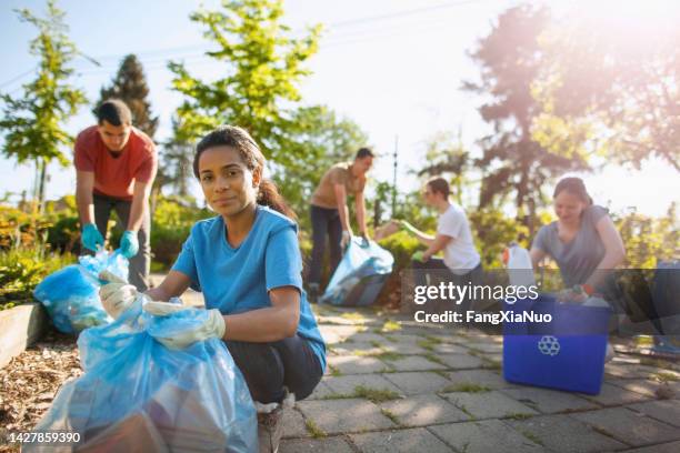 porträt einer hispanischen jungen studentin, die beim aufräumen und recyceln von papier- und plastikflaschen im öffentlichen park des gemeinschaftsgartens mit einer multirassischen gruppe von freiwilligenorganisationen im sommer hilft - umweltschutz reinigungsaktion stock-fotos und bilder