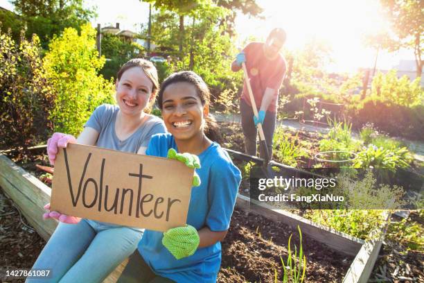 portrait of hispanic young woman and caucasian young woman students hold volunteer sign together in success support achievement determination as youth organization volunteer charity in local community garden in residential district in summer - 青少年組織 個照片及圖片檔