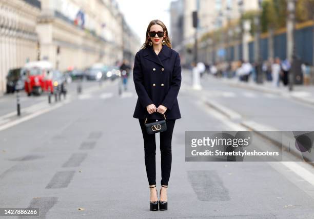 Alexandra Lapp wearing a navy colored caban jacket by Valentino, black skinny pants with gold buttons by Balmain, a black and gold small garavani...