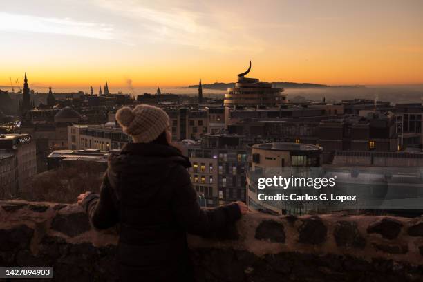 asian woman  admiring the view of edinburgh city's skyline from calton hill during a misty sunset with a dramatic red sky and low clouds in scotland, united kingdom - edinburgh foto e immagini stock