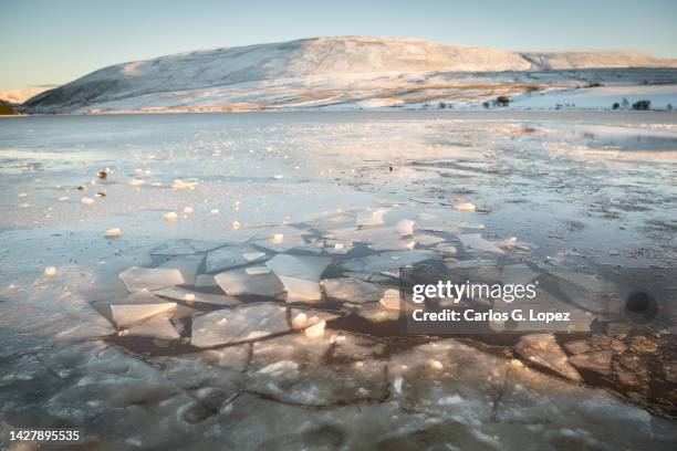 hills covered in snow reflected on the calm icy water of one of the reservoir in the pentland hills regional park in edinburgh, scotland, uk - breaking the ice photos et images de collection