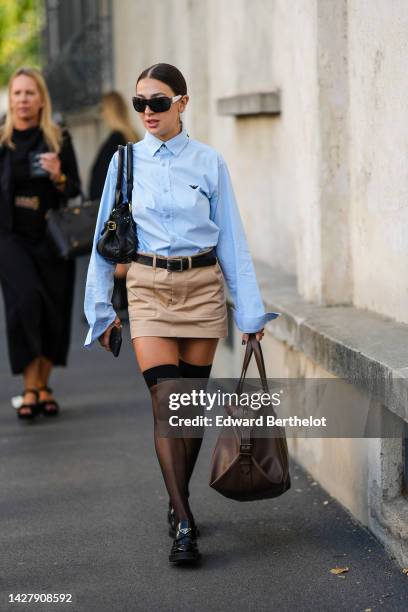 Guest wears black sunglasses, silver earrings, a silver piercing, a pale blue shirt from Emporio Armani, a black shiny leather belt, a black shiny...