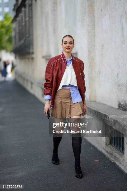 Guest wears a pale blue and black striped print pattern shirt, a matching blue and navy blue striped print pattern belt bag, a burgundy shiny leather...