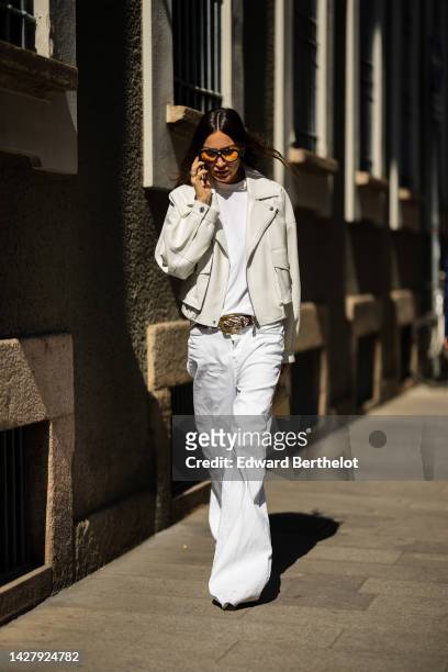 Guest wears black and yellow sunglasses, diamonds rings, a white t-shirt, a white latte leather biker jacket, a brown and white braided leather belt,...