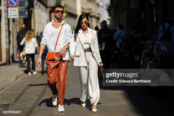 Guest wears brown sunglasses, a white tank-top, a white shirt, an orange shiny leather crossbody bag, camel shiny leather large pants, white leathers...