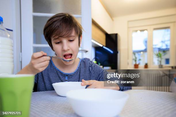 preadolescent boy eating cereal with milk at the dining table at home - boy eating cereal stock pictures, royalty-free photos & images