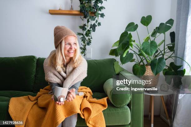 woman in woolen hat sitting on sofa with hot tea - winter sofa stock pictures, royalty-free photos & images