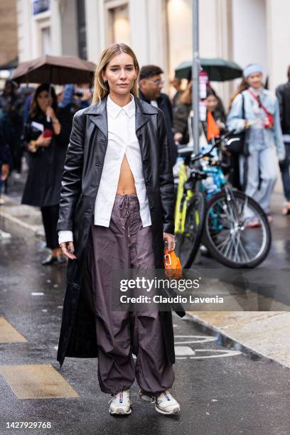 Chiara Capitani is seen wearing a black leather trench coat, beige Salomon sneakers and white shirt outside the Salvatore Ferragamo show during the...