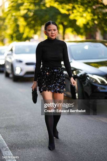 Guest wears a black turtleneck / long sleeves pullover, a black shiny sequined short skirt, a black satin / silk bag, black pointed heels stockings...