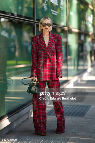 Guest wears black sunglasses, gold and large pearl earrings, a red with black and white checkered print pattern blazer jacket, matching red with...