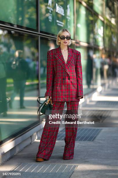 Guest wears black sunglasses, gold and large pearl earrings, a red with black and white checkered print pattern blazer jacket, matching red with...