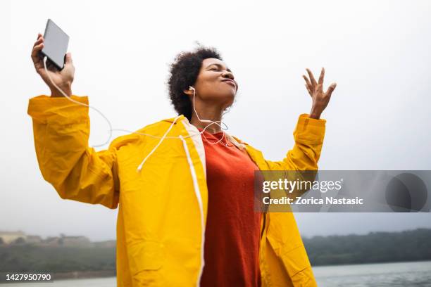 woman wearing yellow raincoat listening music on a rainy day - dancing in the rain stock pictures, royalty-free photos & images