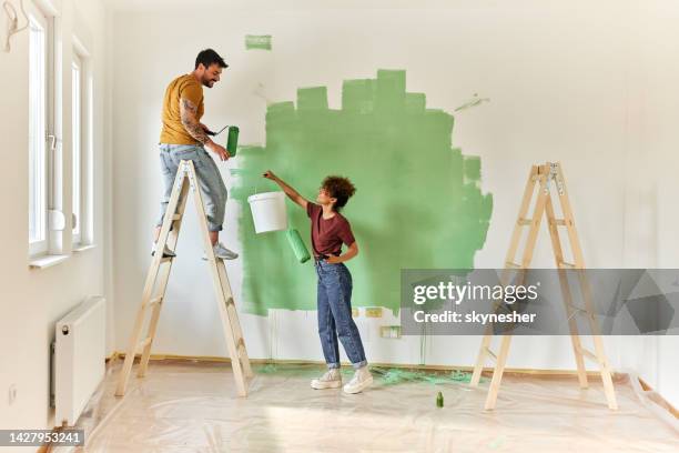 feliz pareja pintando su nuevo apartamento. - handy fotografías e imágenes de stock