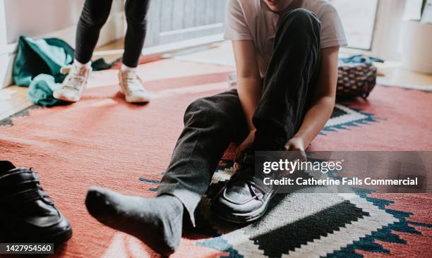a little boy pulls on a velcro fastening shoe before leaving the house for school - vestirse fotografías e imágenes de stock