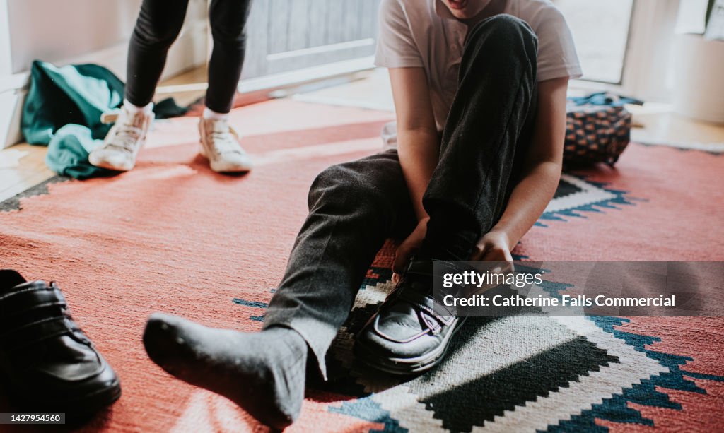 A little boy pulls on a velcro fastening shoe before leaving the house for school