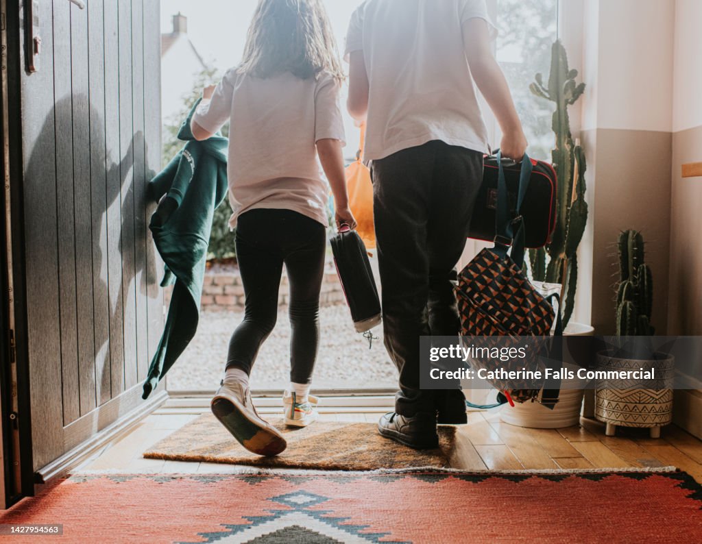 Two young children wearing school uniforms exit their front door