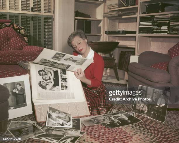 American actress, singer and dancer June Allyson sitting on the floor as she looks at a large scrapbook of press cuttings and publicity stills...