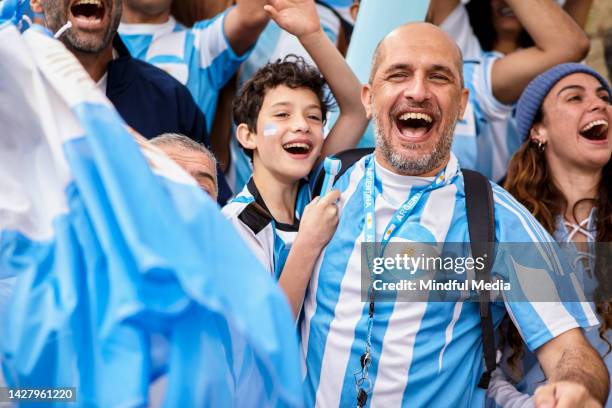 argentinian father and son embracing and cheering while watching football match - argentina football stock pictures, royalty-free photos & images