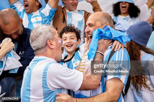 argentinian football fan friends and little boy celebrating goal while standing in the crowd - fans football stockfoto's en -beelden