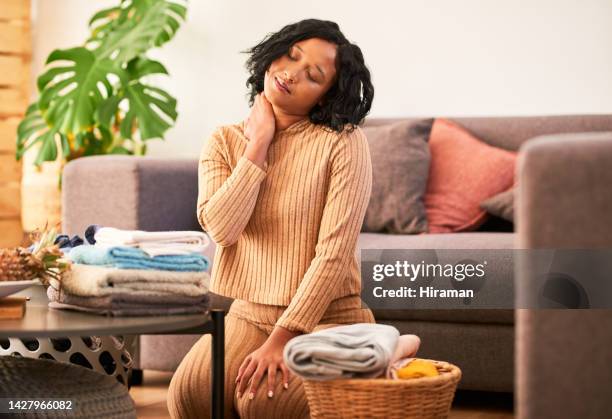 stanco, burnout e dolore al collo della donna che fa il bucato nel suo salotto di casa. ragazza impegnata con stress da lavoro domestico e muscoli doloranti o infiammazione dopo aver piegato vestiti o vestiti nel salone del suo appartamento - male house cleaner foto e immagini stock