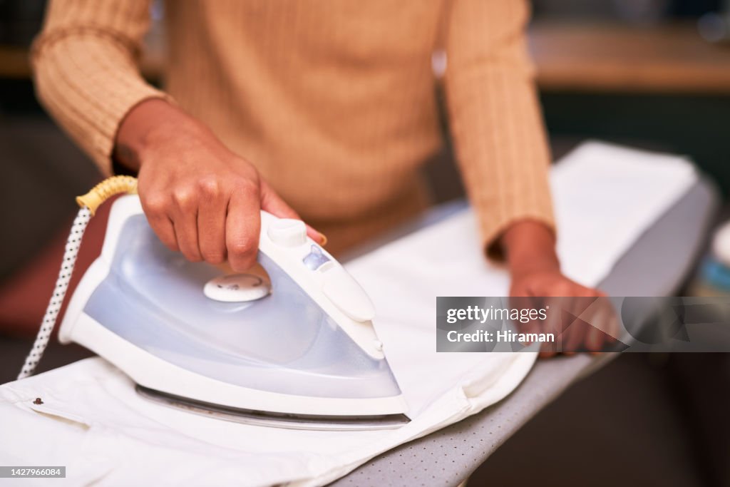 Hand, iron and shirt with the hands of a cleaner woman ironing clothes on a board in a home for cleaning or chores. Laundry, fabric and lifestyle with a female using an appliance for clothing