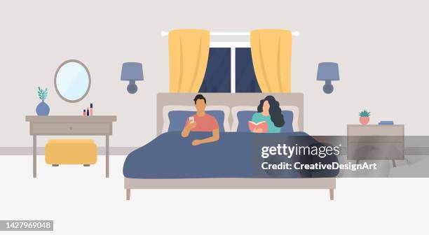 modern bedroom interior with young couple sitting on bed. woman reading book and man looking at his phone - sconce stock illustrations