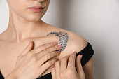 Woman applying cream onto tattoo on her skin against light background, closeup