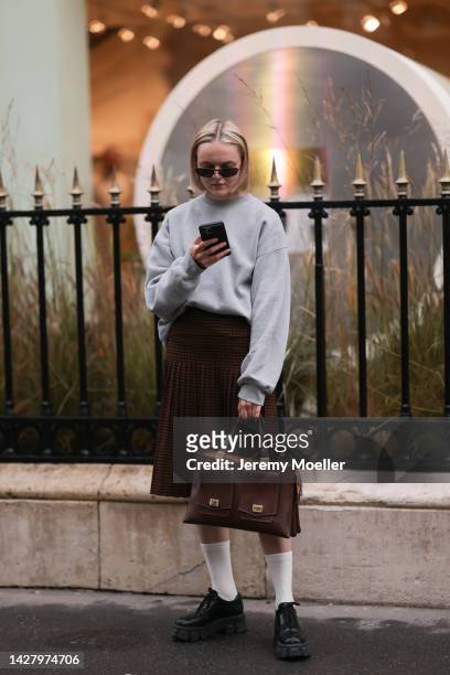 Fashion week guest seen wearing a brown pleated skirt and oversize grey sweater with pleateau black sneaker, outside Jacquemus store opening during...