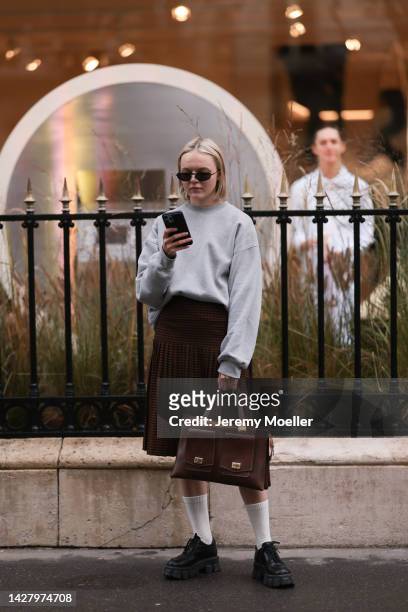 Fashion week guest seen wearing a brown pleated skirt and oversize grey sweater with pleateau black sneaker, outside Jacquemus store opening during...