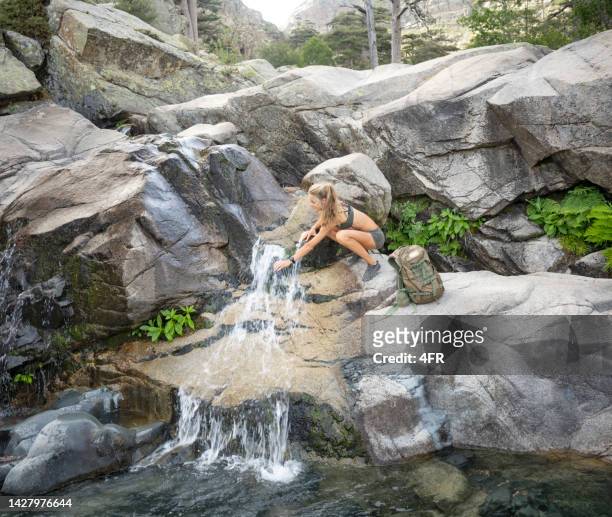 beautiful woman hiking filling up her water bottle at a natural waterfall on the island corsica, france - cascade france stock pictures, royalty-free photos & images