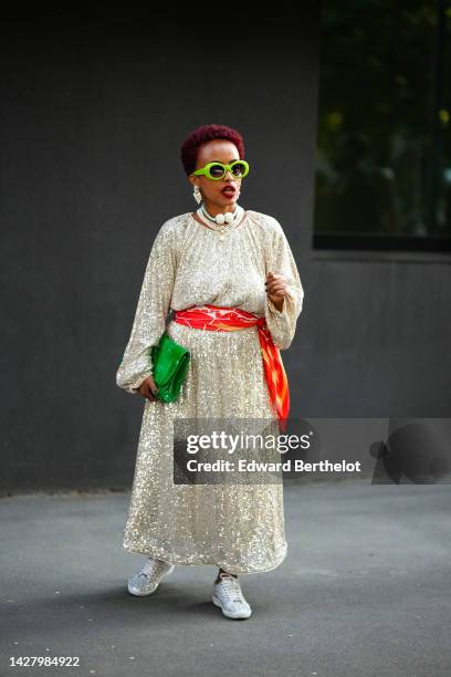 Guest wears neon green sunglasses, white pearls pendant earrings, white pearls necklaces, a white sequined long sleeve / long dress, a red / orange /...