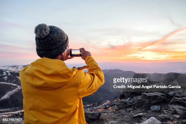 man hiking on vacation taking picture with phone - yellow coat stock-fotos und bilder