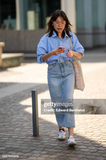 Guest wears glasses, earrings, a pale blue with white striped print pattern shirt, a blue faded high waist long skirt, a white with pink print...