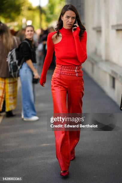 Guest wears a neon red cut-out shoulder / long sleeves / turtleneck pullover, a black shiny leather flared pants with nailed / studded belt, red...