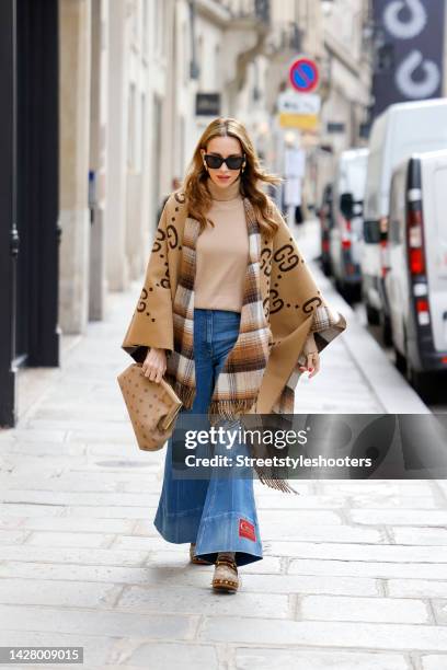 Alexandra Lapp wearing a beige poncho by Gucci, a camel colored silk turtleneck pullover by Riani, dark blue flared denim jeans pants by Gucci, a...