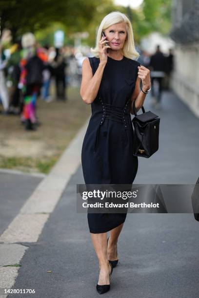 Guest wears a black sleeveless / laces belted midi dress from Prada , a black shiny leather handbag from Prada, a silver Serpenti watch from Bulgari,...