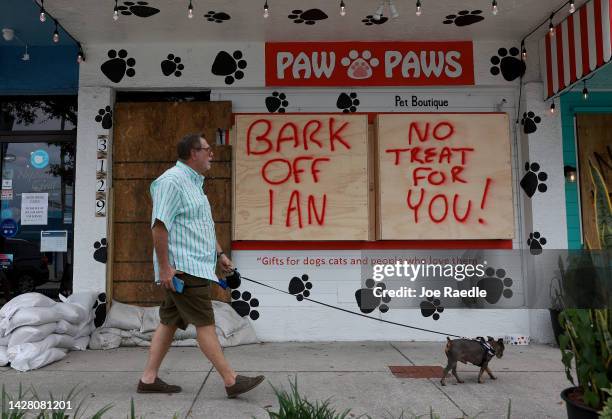 Michael and Romeo walk past a sign reading,' Bark Off Ian, No Treat for you,' painted on a building that is boarded up for the possible arrival of...