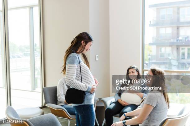 mid adult expectant mom shows friends belly bump - prenatal care stockfoto's en -beelden