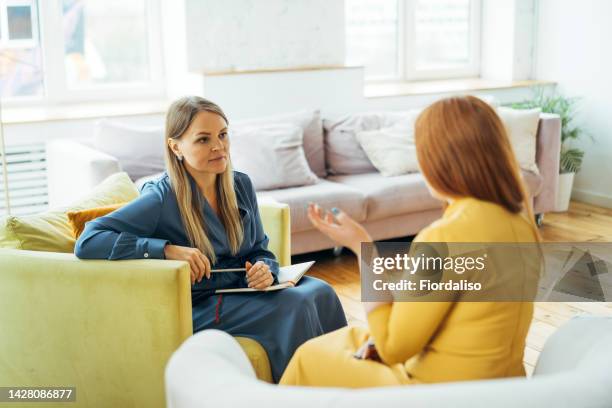 two women sitting in armchairs and talking. woman psychologist talking to patient - stressed young woman sitting on couch stock-fotos und bilder