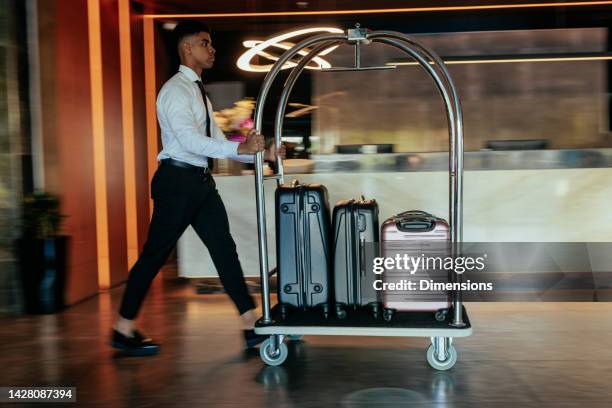 hotel attendant pushing luggage cart. - luxury hotel lobby stock pictures, royalty-free photos & images