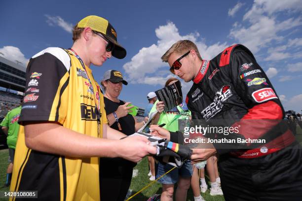 Garrett Smithley, driver of the Trophy Tractor Ford, signs an autographs for a NASCAR fan during pre-race ceremonies prior to the NASCAR Cup Series...