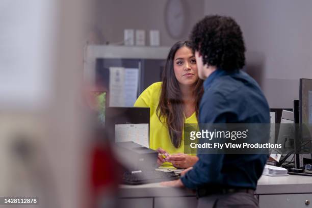 femme latine parlant à la réceptionniste à la banque ou au cabinet médical - guichet de banque photos et images de collection
