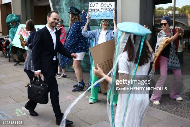 Activists hold placards as they greet a delegate with a morning rave outside the International Maritime Organization at the start of the 80th Marine...