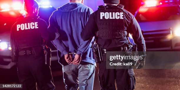 handcuffed suspect being arrested by police at night - arrest warrant stock pictures, royalty-free photos & images