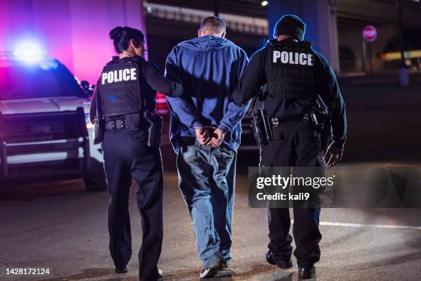 handcuffed suspect being arrested by police at night - black police stock pictures, royalty-free photos & images